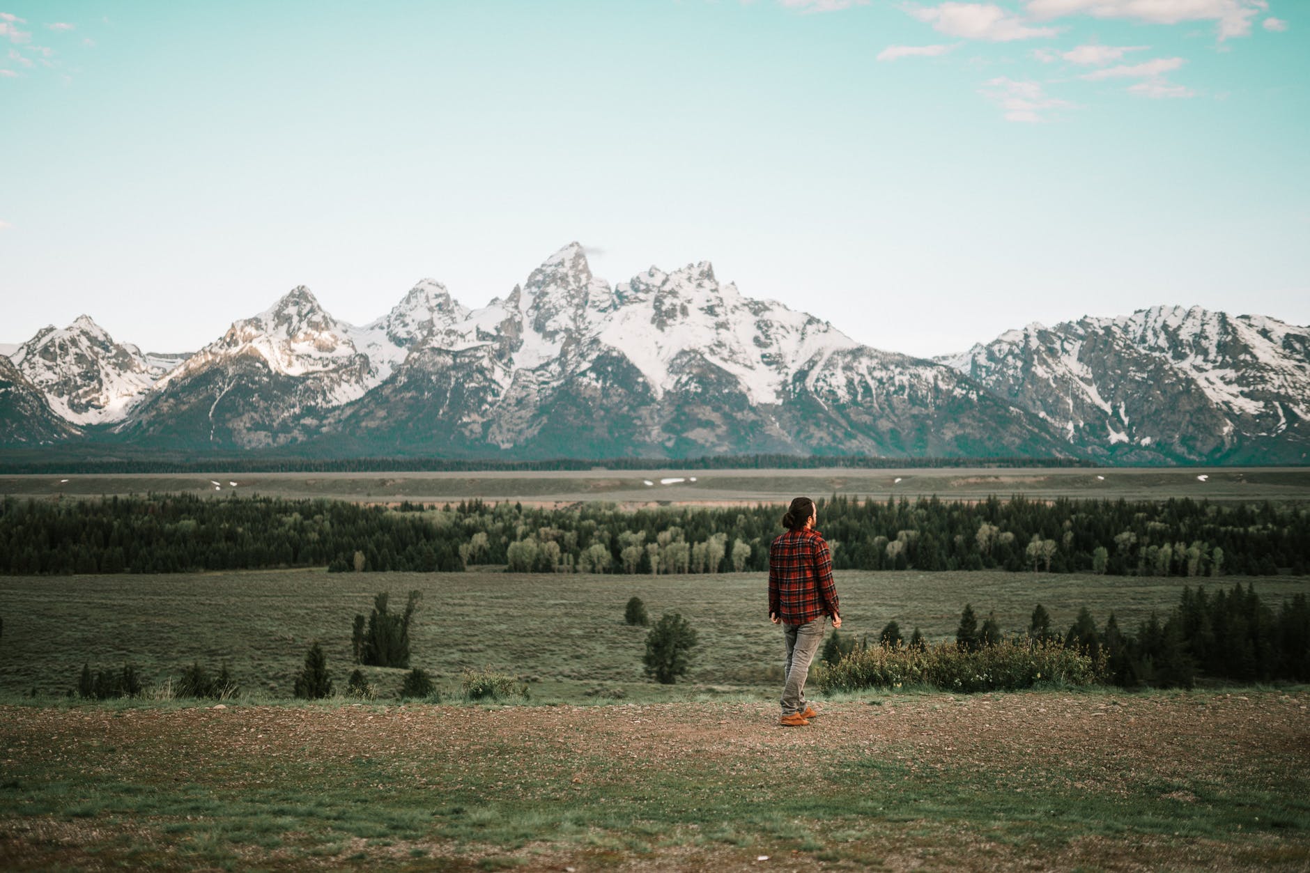 person in red jacket standing on green grass field near snow covered mountain
